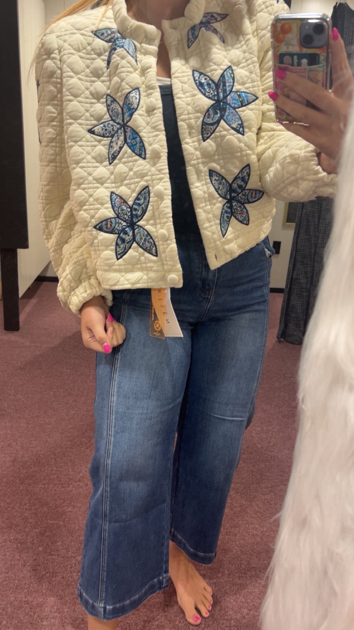 Person wearing a cream quilted jacket with blue floral patterns and blue jeans, standing in a store.